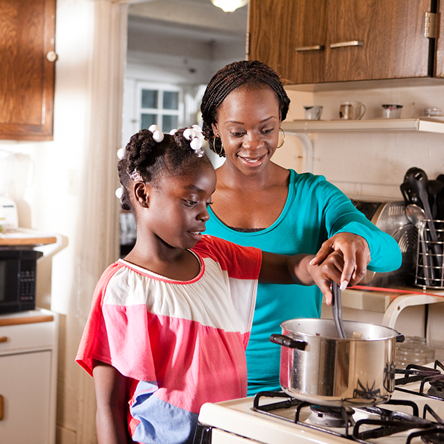 Champion mom assisting daughter with cooking on the stove