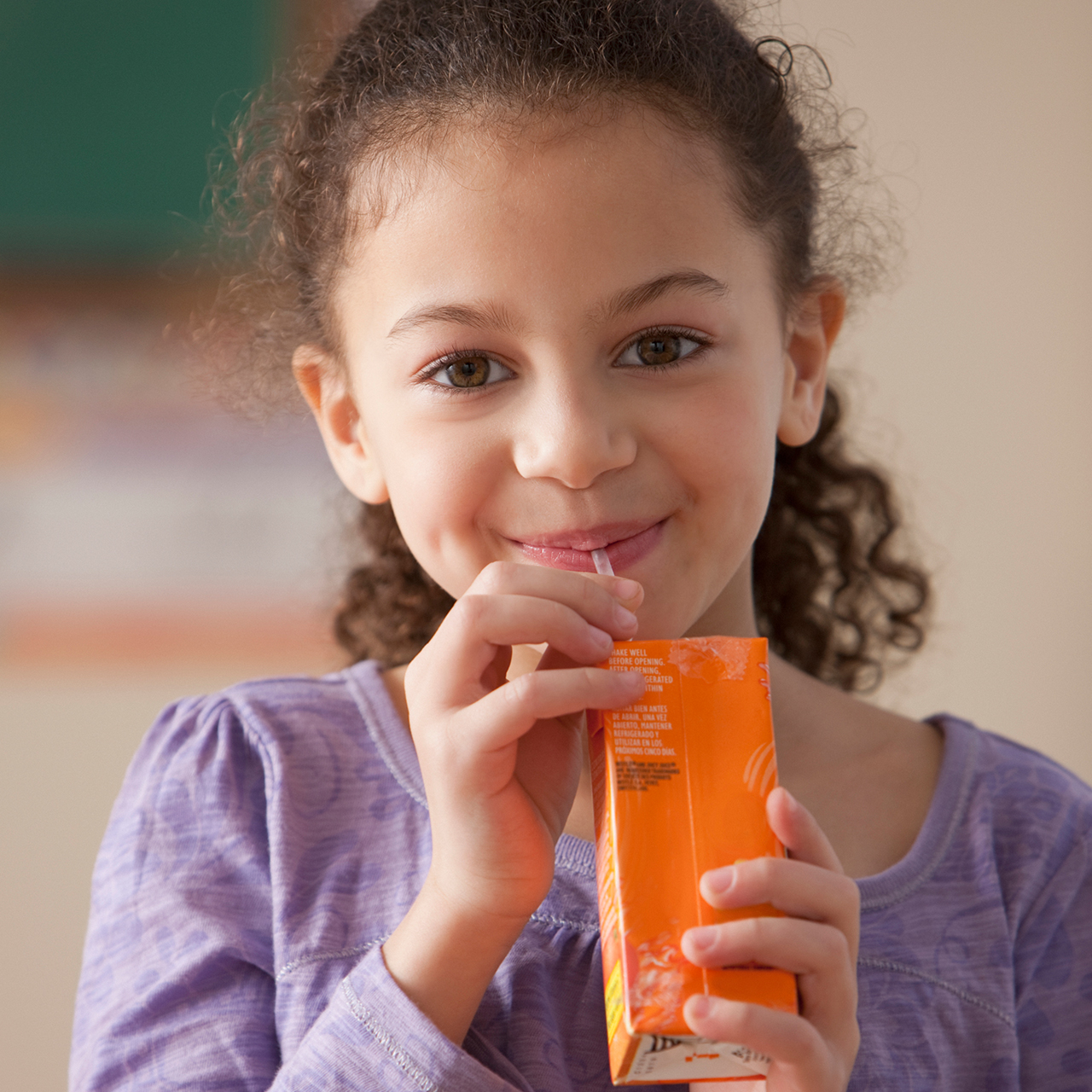 Una niña sonriente bebiendo jugo en una cajita